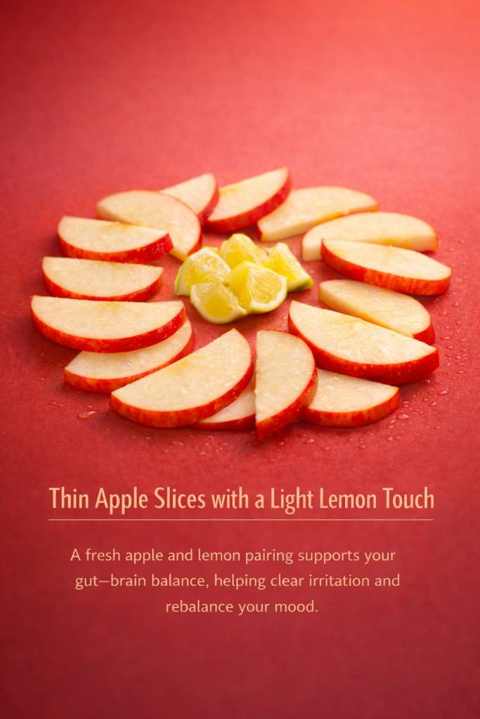 Thin apple slices arranged in a circle with lemon pieces in the center, placed against a red background.